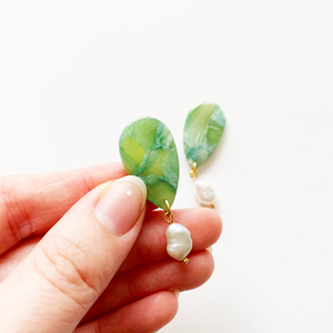 Jade-colored polymer clay earrings with freshwater pearl drop and gold accents. Hand holding earring up to display transparent nature and scale.